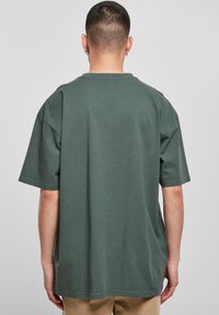 Zöld pamut póló rövid ujjal, kerek nyakkal és laza szabással. Minimalista dizájn, látható minták vagy logók nélkül.
