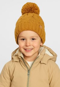 Żółta dziana czapka z dużym pomponem na czubku, z teksturowanym prążkowanym wzorem. Nosi ją dziecko w beżowej kurtce.