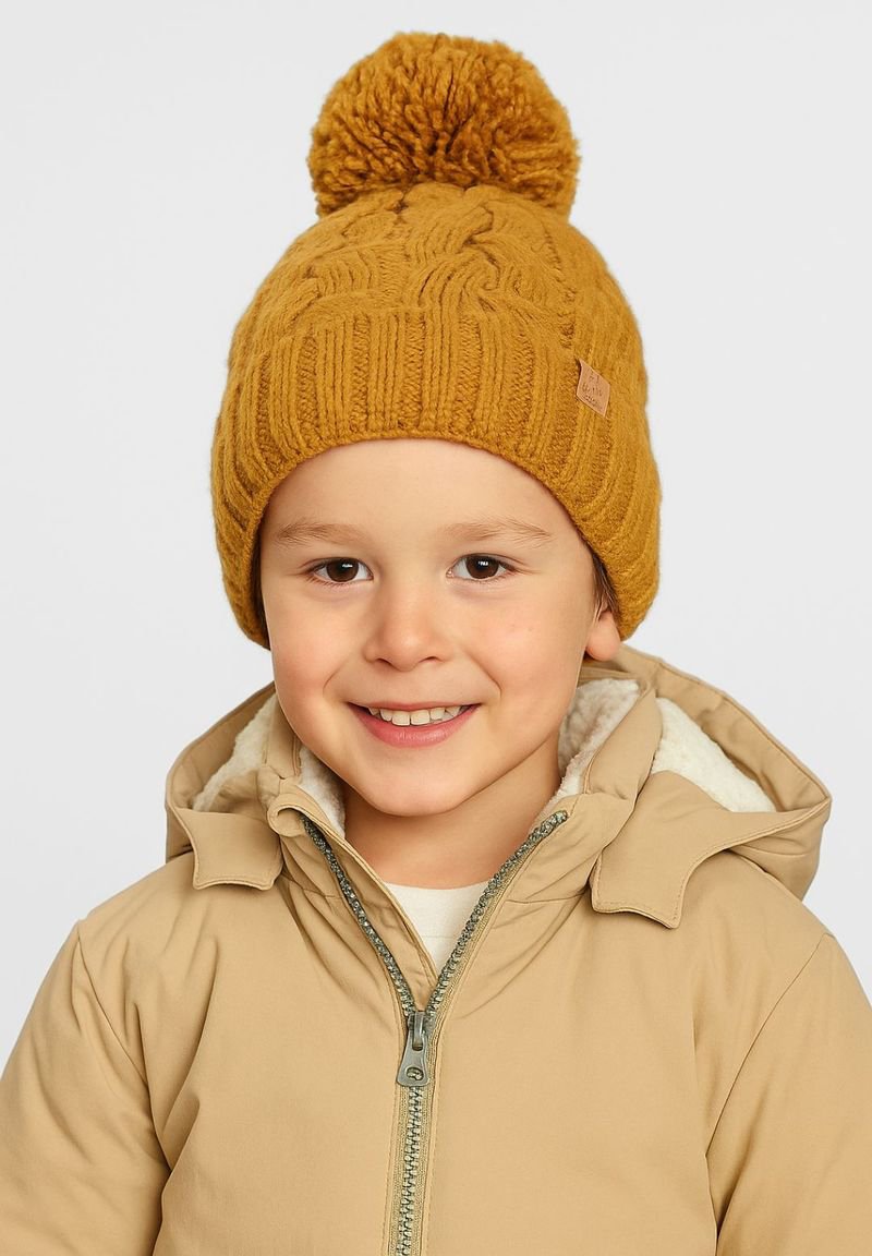 Żółta dziana czapka z dużym pomponem na czubku, z teksturowanym prążkowanym wzorem. Nosi ją dziecko w beżowej kurtce.