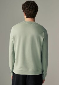 Sudadera verde claro con mangas largas, cuello redondo y puños acanalados. Textura suave, corte casual y detalle de costura plana en el dobladillo.