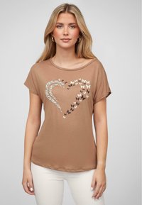 Brun bomulls t-skjorte med et hjerte-design laget av leopardmønster og sommerfugler i krem, brunt og svart. Rund hals, korte ermer.