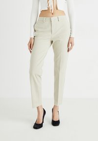 Beesid kohandatud püksid slim fit lõikega, aksenteeritud taskutega ja vöökinnitusdetailidega. Kompositsioonis valge lühiülikond ja mustad kõrged kontsad.
