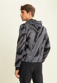 Sudadera con capucha en gris con un patrón de pinceladas abstractas en negro. Presenta una textura suave, puños acanalados y un corte relajado.