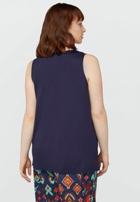 Top senza maniche di colore blu navy realizzato in tessuto morbido, con scollatura tonda e vestibilità rilassata, abbinato a pantaloni colorati e fantasia.