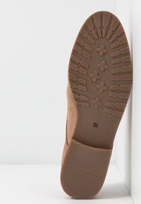 Semelle de bottine en daim marron avec une surface en caoutchouc texturée présentant divers motifs, les chiffres embossés "36" et un design à bout arrondi.