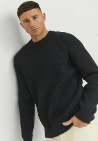 Maglione in maglia a coste navy con collo rotondo e maniche lunghe. Presenta una texture spessa e una vestibilità rilassata. Esibito su uno sfondo neutro.