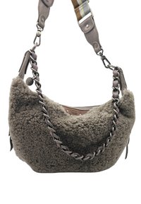 Sac à main en shearling gris avec une bandoulière tressée, doté d'une fermeture éclair et d'un intérieur en daim marron. Les accents comprennent des éléments métalliques et des détails texturés.
