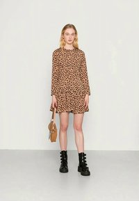Vestido mini de manga longa com padrão de leopardo e bainha rodada, feito de um tecido suave. Estilizado com botas de combate pretas e uma pequena bolsa castanha.