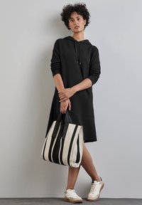 Robe sweat noire avec une coupe ample et des manches longues, associée à un sac fourre-tout noir et blanc rayé et des baskets légères. Texture lisse.
