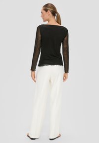 Czarna bluzka z długim rękawem z przezroczystej tkaniny i falbaniastym dołem, połączona z białymi spodniami o szerokich nogawkach. Gładka tekstura, minimalistyczny design.