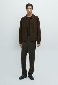Brun uld zip-up jakke, parret med en mørkebrun ribbet sweater og løse brune bukser. Sorte snørebåndssko fuldender outfittet.