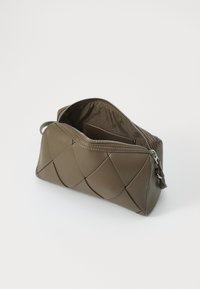 Sacca in pelle verde oliva con design trapuntato, chiusura con zip e marchio interno. Forma compatta con texture liscia e dettagli in metallo argentato.