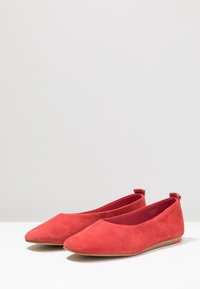 Ballerines en daim rouge à bout pointu, talon plat et doublure en tissu. Texture lisse avec un design minimaliste et sans quincaillerie visible.