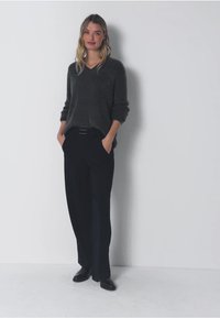 Maglione grigio a maglia con scollo a V, abbinato a pantaloni larghi scuri e scarpe nere. Il tessuto è morbido, con una vestibilità rilassata e maniche lunghe.