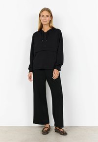 Sweatshirt à capuche léger noir au design court, avec une patte de boutonnage et une poche avant, associé à un pantalon large noir.