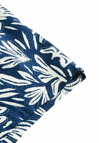 Kék és fehér mintás textil, levelek mintájával. Textúrált szövés, látható széllel és varrási részletekkel. Kész varráshoz vagy kézműveskedéshez.