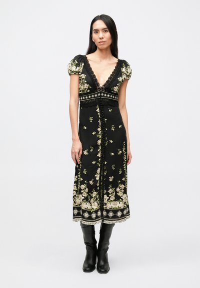 Μαύρο φόρεμα με floral σχέδιο, με φουσκωτά μανίκια, βαθύ V-ντεκολτέ, δαντελένιες λεπτομέρειες και κεντήματα κατά μήκος του τελειώματος· συνδυασμένο με μαύρα μποτάκια μέχρι το γόνατο.