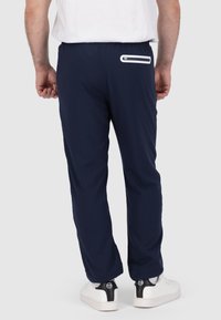 Marineblauwe sportbroek gemaakt van een soepele, lichte stof. Voorzien van een witte ritszak aan de achterkant en een elastische tailleband.