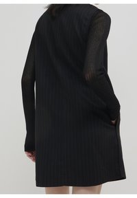 Svart randig klänning med ärmlös design, som har ribbade svarta långa ärmar, sidofickor och rak nederkant.