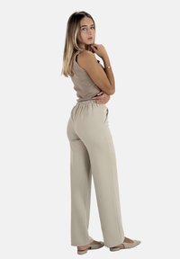 Beige elastisk midja vida byxor och en ribbad beige linne. Modellen står i profil och visar upp outfitens enkla design och passform.