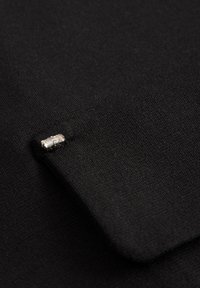 Tissu noir à texture lisse, présentant un bord plié et un petit accent en strass clair fixé.