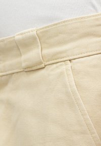 Beżowe bawełniane szorty o fakturowanym wykończeniu, z pasem, szlufką na pasek i bocznymi kieszeniami, z widocznym szczegółowym przeszyciem.