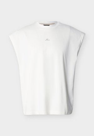 White sleeveless oversized shirt with small black Nike logo and "Nike Standard Issue" text centered below the neckline.