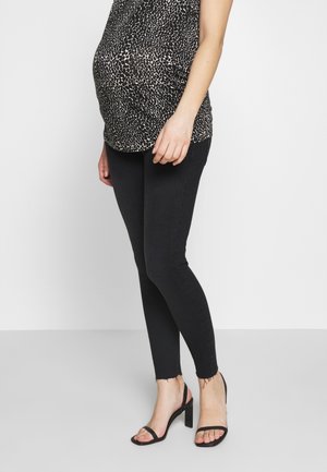 Těhotná osoba oblečená v černobílém vzorovaném topu, černých úzkých džínách s třepenými lemy a černých sandálech na vysokém podpatku.