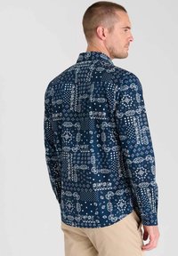 Marineblauwe longsleeve shirt met een gevarieerd wit patroon, waaronder bloem- en geometrische ontwerpen. Klassieke kraag en met knopen sluitende manchetten.