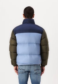 Prošívaná bunda v modré, námořnické modři a olivově zelené barvě. Má vysoký límec, prošívanou strukturu a elastické manžety. Nositelná přes džínové kalhoty.