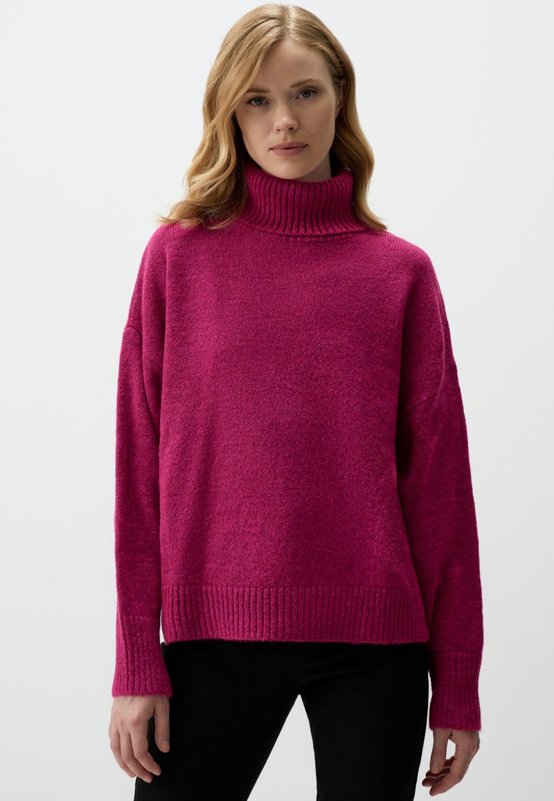 Pull en maille magenta avec col roulé, coupe ample, poignets et ourlet côtelés. Texture douce avec une conception décontractée, mettant en avant des épaules tombantes.