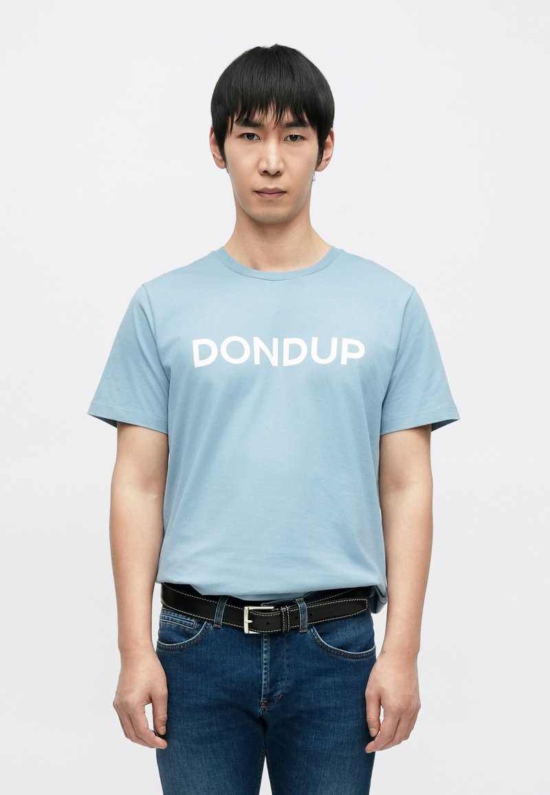 Ανοιχτό μπλε βαμβακερό μπλουζάκι με λευκά γράμματα "DONDUP", κοντά μανίκια, στρογγυλή λαιμόκοψη, συνδυασμένο με σκούρα τζιν και μαύρη ζώνη.