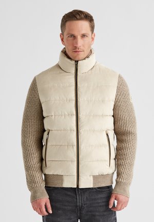 Gepolsterte Weste in hellem Creme mit hohem Kragen, ausgestattet mit texturierten beigen Ärmeln und gerippten Bündchen, Reißverschluss und seitlichen Taschen.