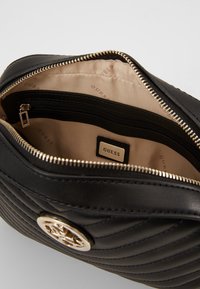 Sort quiltet læder Guess taske med guldlogo, beige indvendig foring og lynlåslomme indeni.