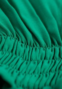 Elastische groene stof met een geraffineerde textuur, waarin een ribpatroon zichtbaar is. Het oppervlak lijkt glad met een consistente, levendige kleur.