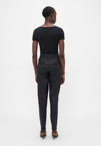 Haut noir ajusté et pantalon en cuir noir élégant avec taille élastique, présentant une texture lisse et une silhouette épurée. Des chaussures à talons hauts complètent le look.