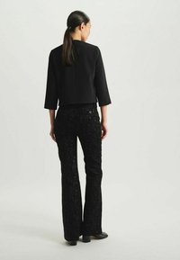 Veste noire raccourcie à manches trois-quarts associée à un pantalon évasé noir en sequins. Les deux pièces présentent une texture lisse et un design ajusté.