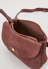 Zamszowa mini torebka w głębokim burgundzie z złotymi zamkami i elementami. Posiada jeden pasek i zapięcie na klapkę. Wnętrze wykończone podszewką.