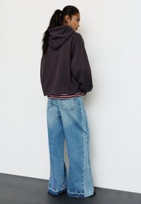 Ylimittainen tummanharmaa huppari hupulla, yhdistetty vaaleansinisiin leveälahkeisiin farkkuihin, joissa on rispaantunut helma ja teksturoitu denim.