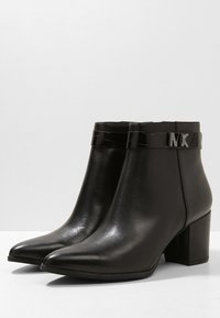 Schwarze Knöchelstiefel aus glattem Leder mit spitzem Zeh, glänzendem schwarzen Akzentband und einem Blockabsatz mit metallicfarbener Logodetail.