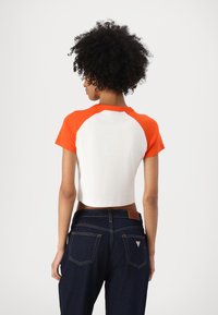 Cropped T-shirt with orange raglan sleeves and a white body. Paired with dark blue denim jeans, featuring a leather tag on the waistband.
