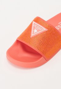 Korallsandal med strassbeströdd rem, med en vit triangel-logotyp och texturerad fotbädd för komfort.