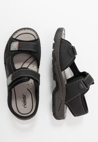 Svarta sandaler med justerbara remmar och grå accenter. Texturerad fotbädd och grov yttersula. Har röda sömmar och sidöppningar.