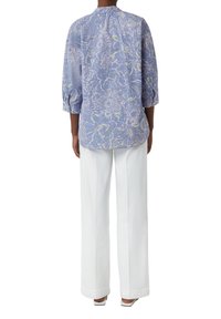 Floral-patterned blue blouse with three-quarter sleeves and a rounded hem, paired with white wide-leg trousers. Smooth fabric texture.