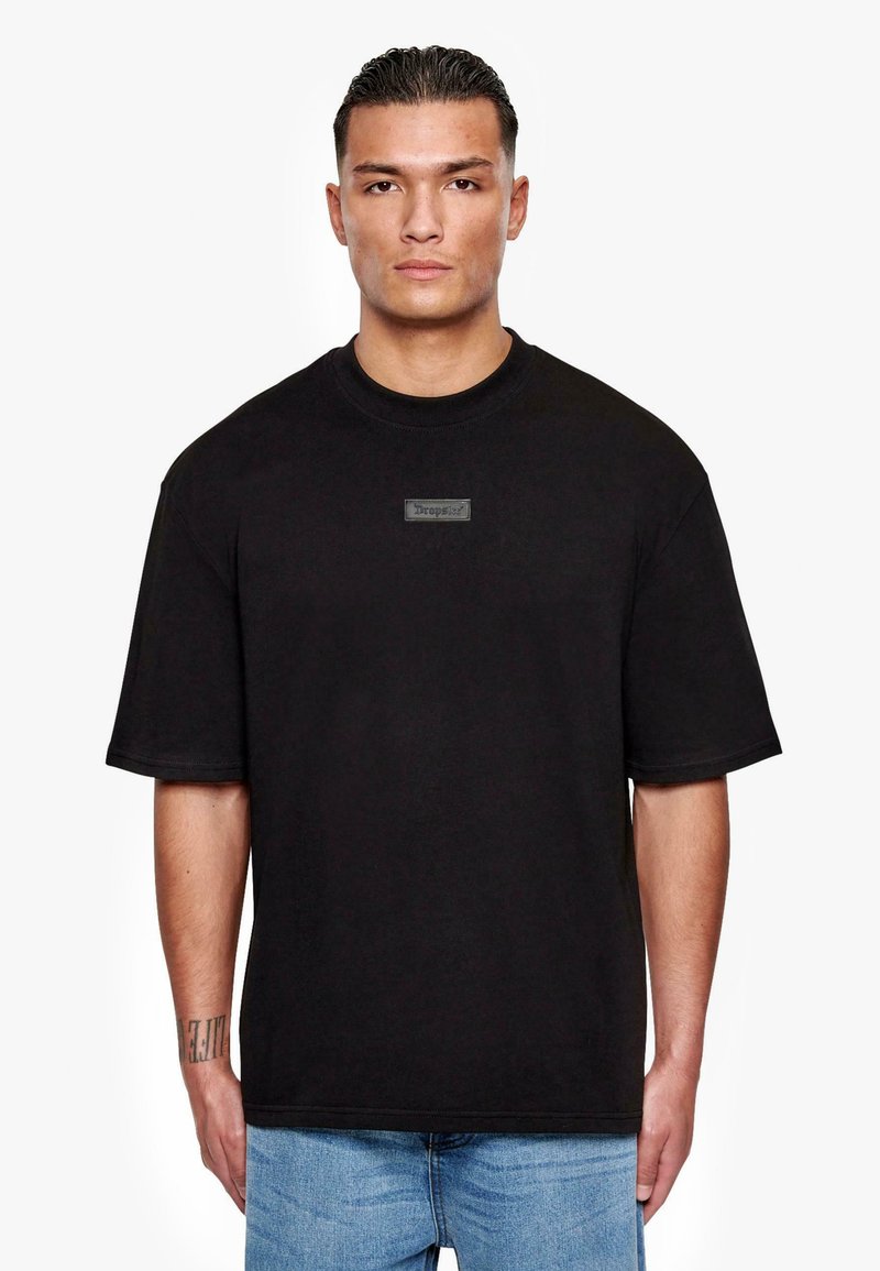 Black cotton t-shirt with a round neck and short sleeves, featuring a rectangular label with the word "Drops" on the front.