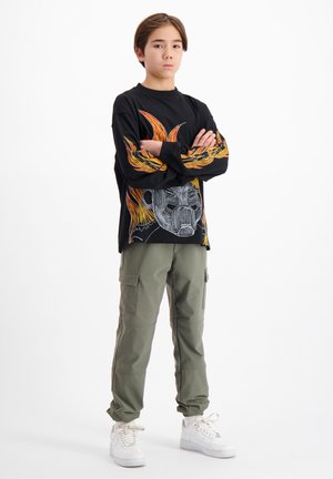 Zwart langamige T-shirt met kleurrijke grafische ontwerpen op de mouwen en de voorkant, gedragen met olijfgroene cargobroek en witte sneakers.