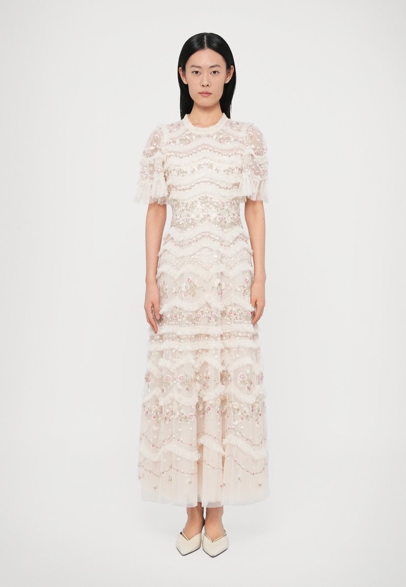 Dlhé, viacvrstvové šaty z priesvitnej svetloružovej látky s kvetinovou výšivkou. Majú nariasené rukávy a ozdobné volány po celej dĺžke. Špicaté topánky.