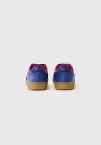 Par tenisica Nike niskog profila u plavoj i crvenoj boji s gumenim potplatima, prikazanih odostraga na praznoj bijeloj pozadini.