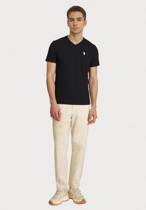 Zwart T-shirt met V-hals van katoen, met een klein wit logo op de linkerborst, gecombineerd met licht crèmekleurige chino's en beige sneakers.