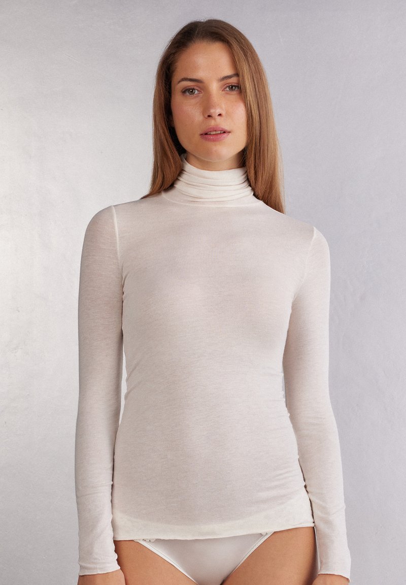 Långärmad polokrage-topp i ljusbeige, tillverkad av ett mjukt, semi-genomskinligt material med en figurnära design och sömlig finish vid fållen.